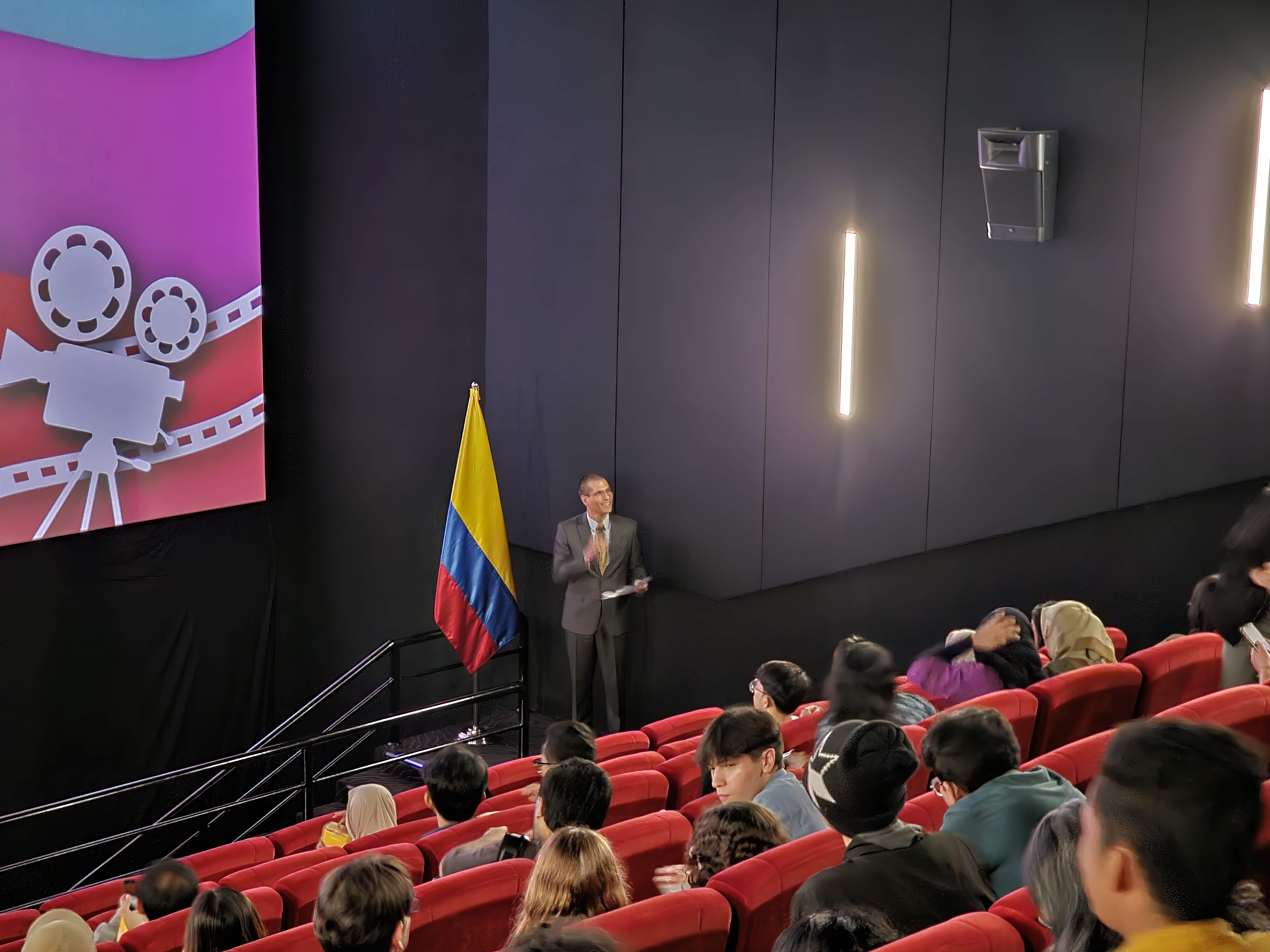 Encargado de Negocios a.i. de la Embajada de Colombia, Carlos Dueñas frente al público asistente agradeciendo la participación de los presentes y dando las palabras introductorias sobre la película.